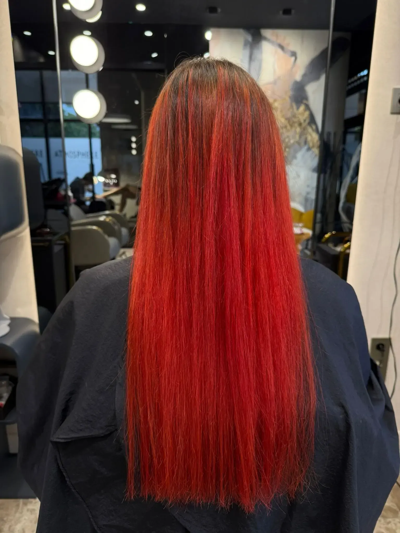 Vista posterior de una persona con cabello largo, liso y rojo, oscuro en las raíces, en un salón de belleza.