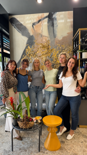 Cinco personas posando en el interior junto a un gran cuadro abstracto, con plantas y un taburete amarillo delante.