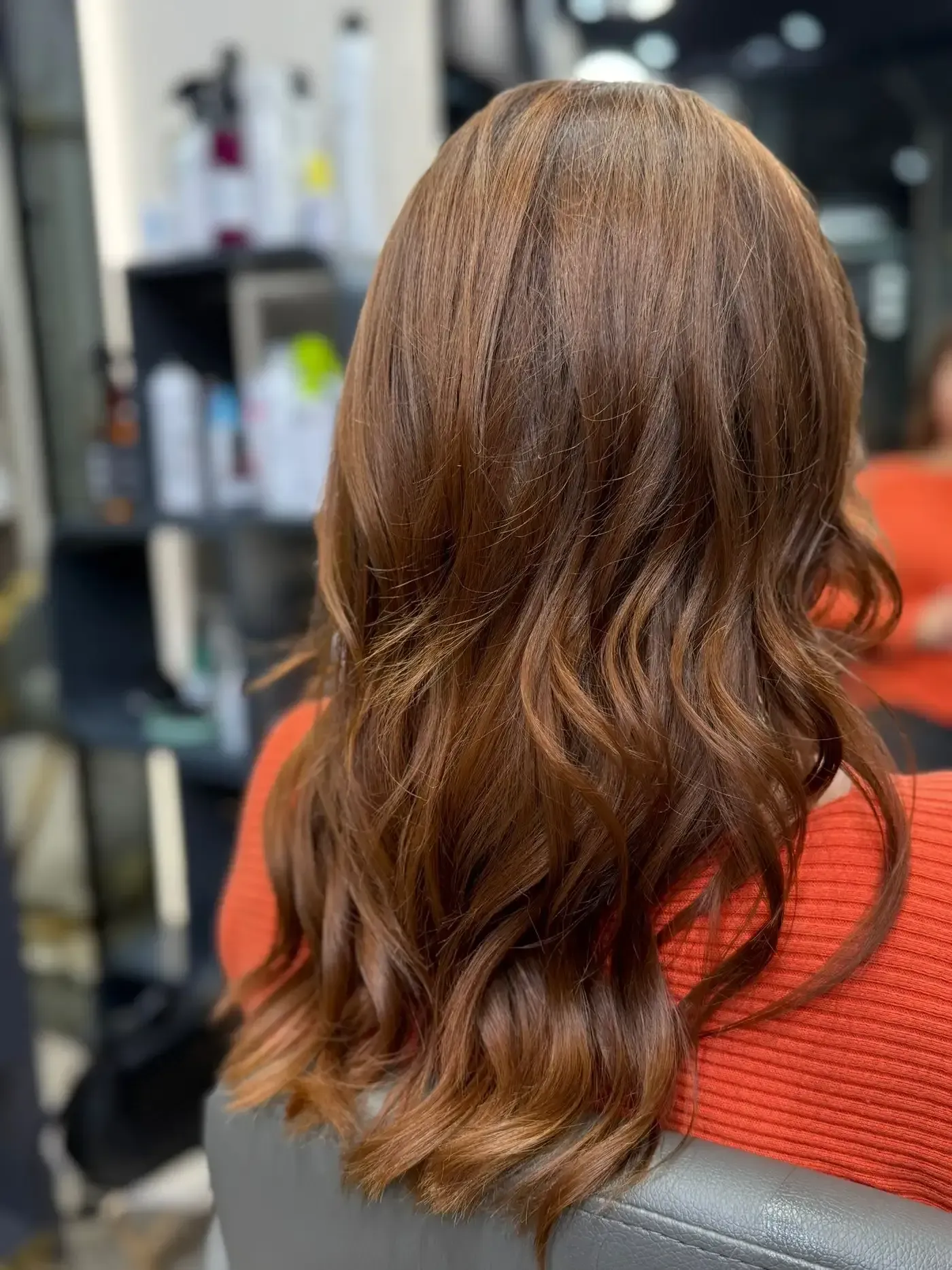 Mujer con cabello castaño largo, ondulado en una silla de salón.