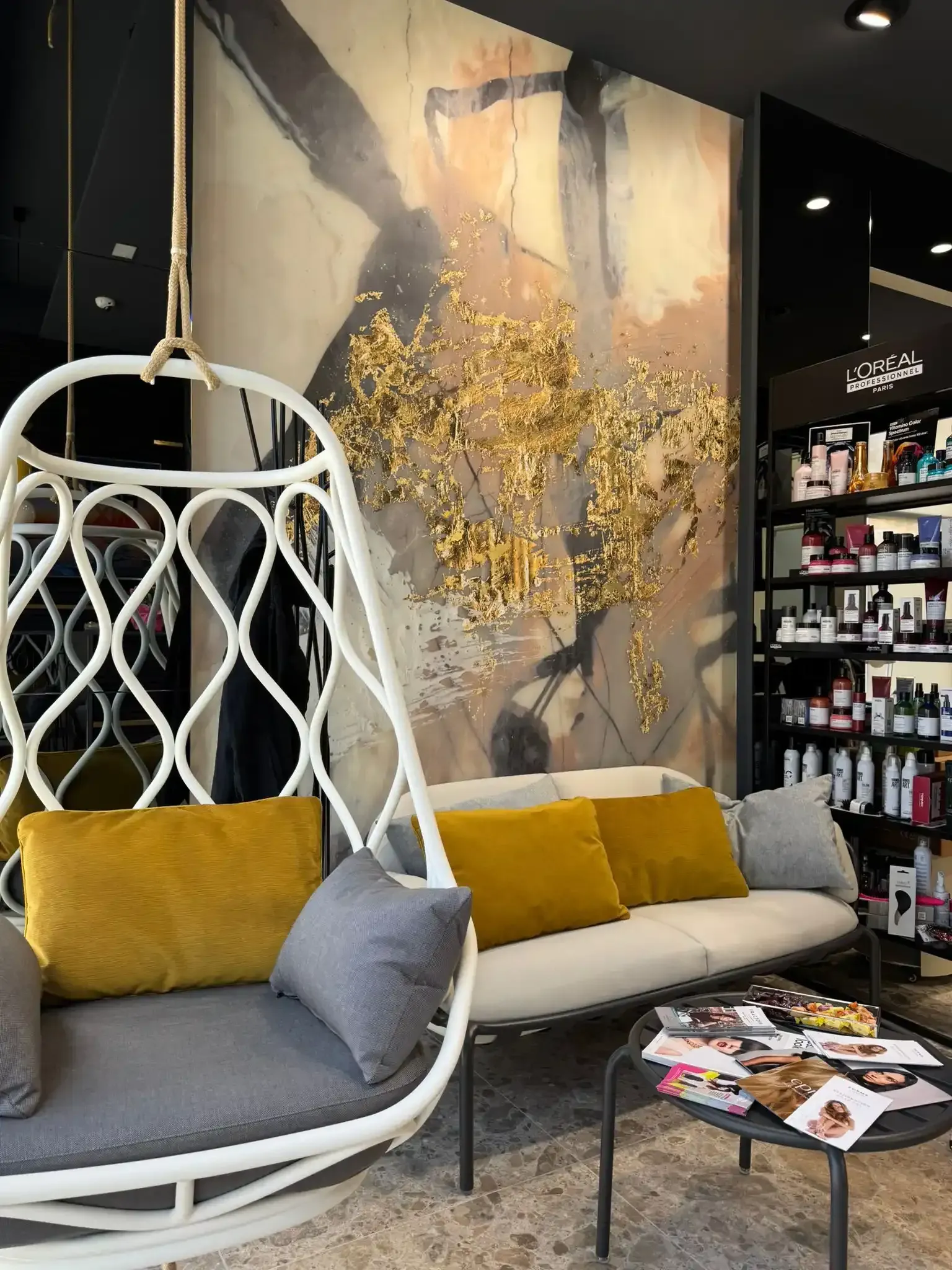 Acogedora sala de estar con sillón colgante y sofá, detalles dorados y obras de arte abstractas.