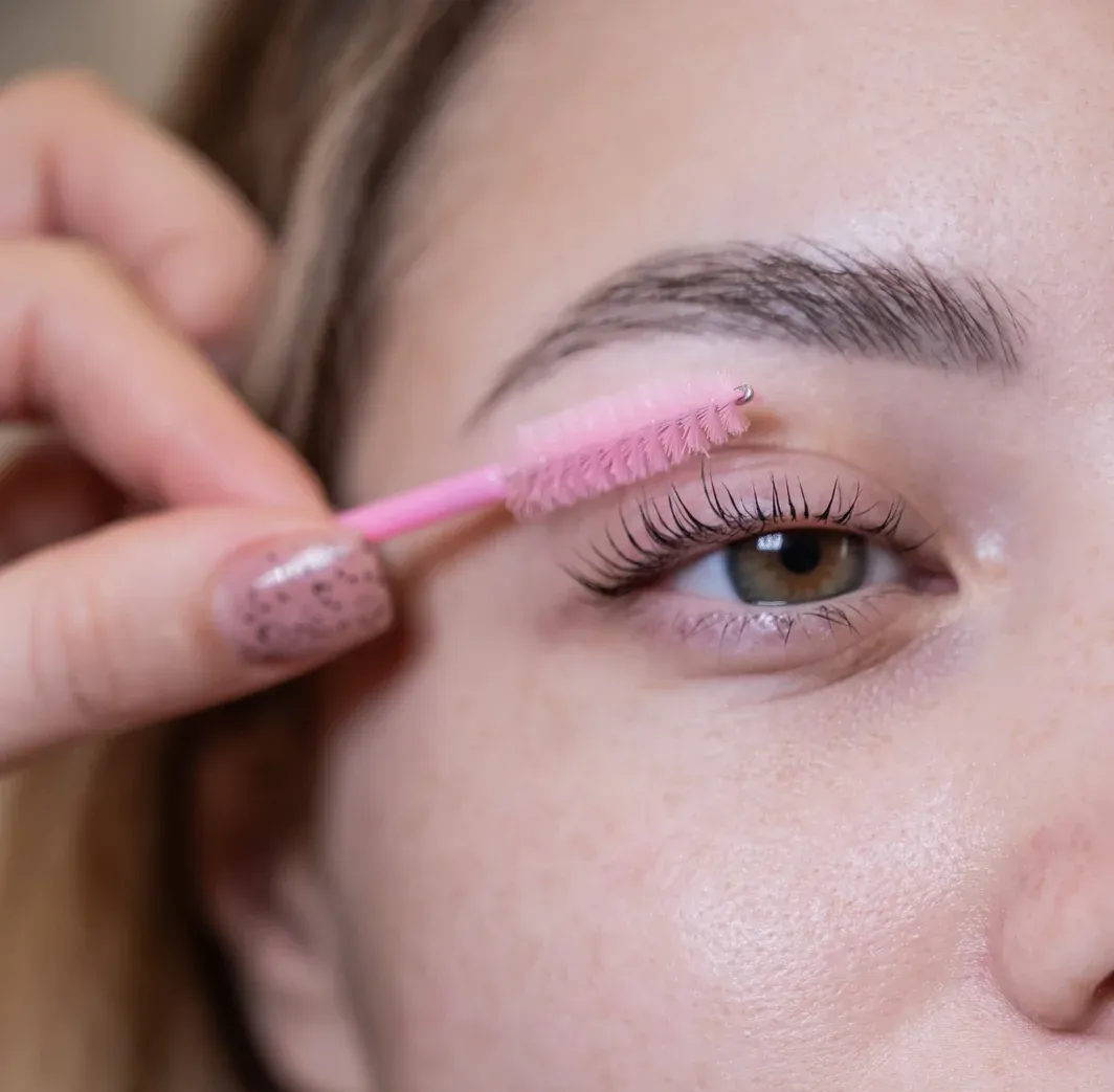 Una persona que utiliza un aplicador de rímel rosa en sus pestañas; primer plano.