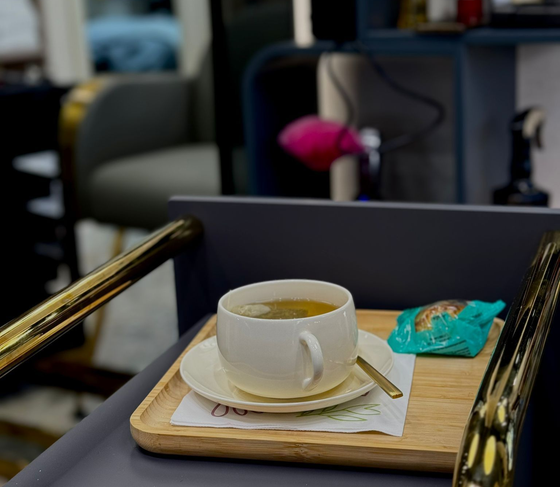 Taza de té en una bandeja de madera con un dulce. Decoración de peluquería, silla con detalles dorados.