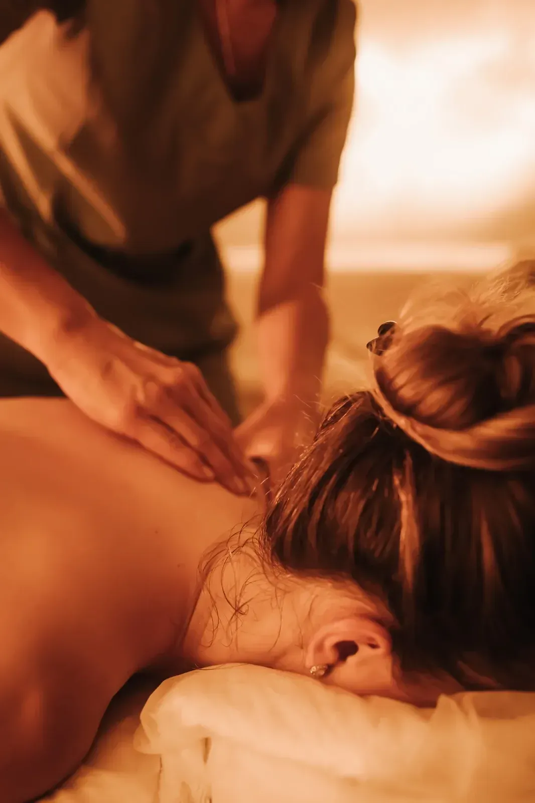 Persona recibiendo masaje de espalda, manos del masajista en la espalda, iluminación suave.