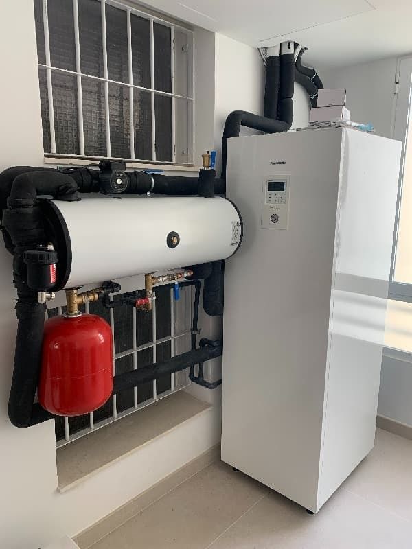 Un calentador blanco está sentado en una habitación al lado de una ventana.