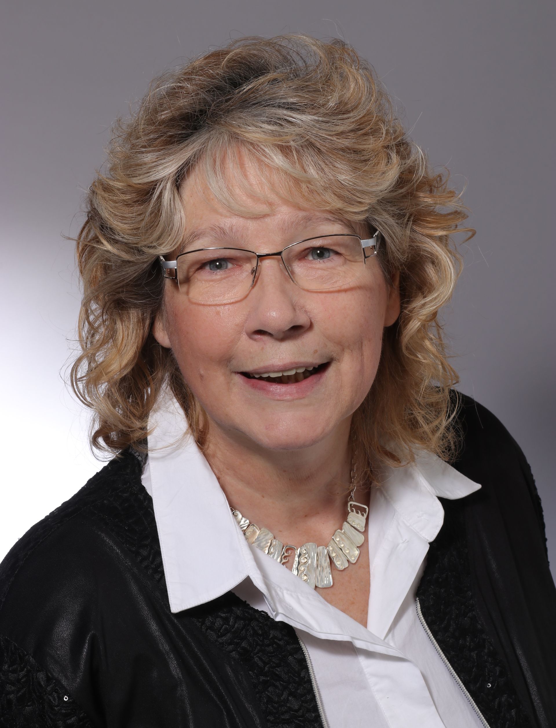 Eine Frau mit Brille und Halskette lächelt in die Kamera.