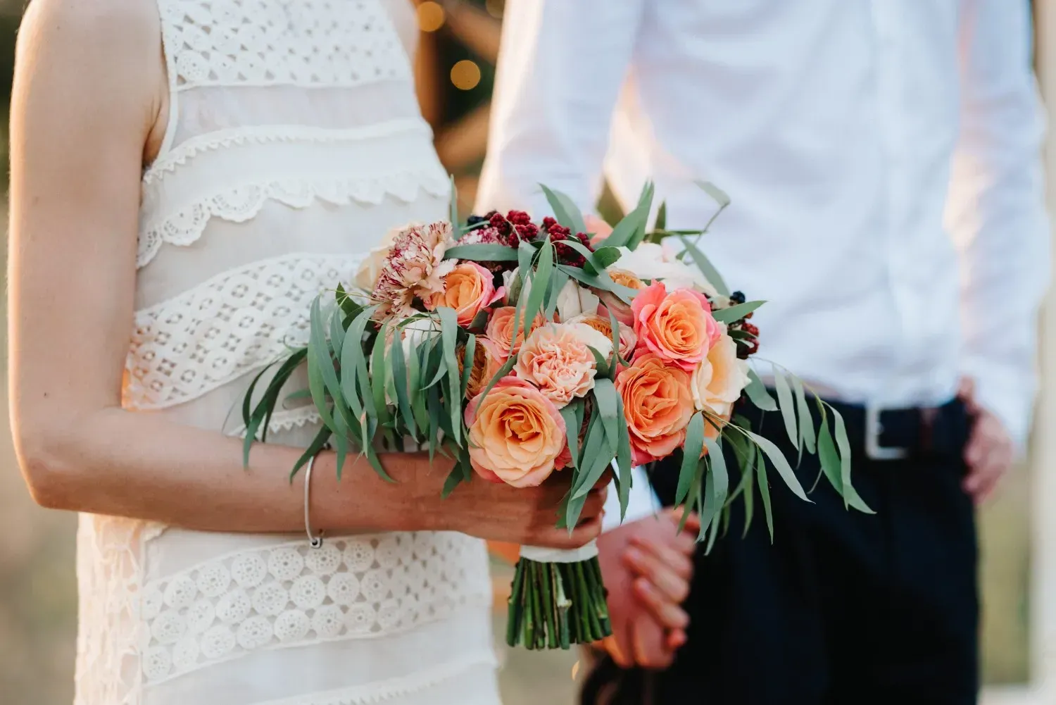 Una mujer vestida con un vestido de encaje blanco sostiene un ramo.