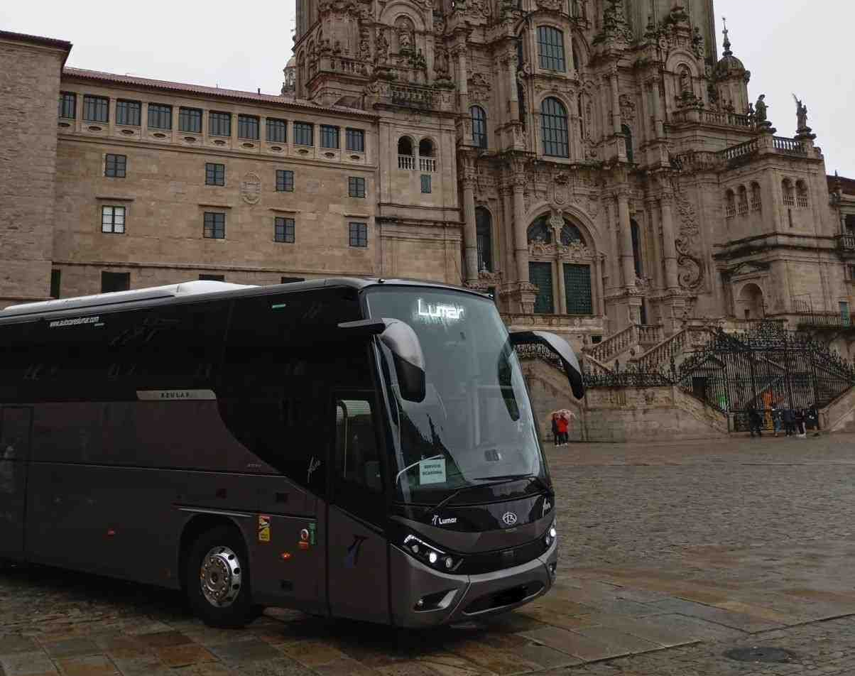 Un elegante autobús turístico de color gris oscuro estaba estacionado frente a la arquitectura curvilínea.