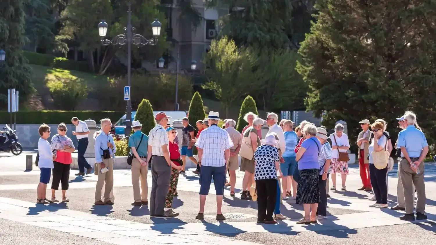Un grupo diverso de turistas permanece de pie al aire libre en una soleada plaza pavimentada durante una visita guiada a pie.