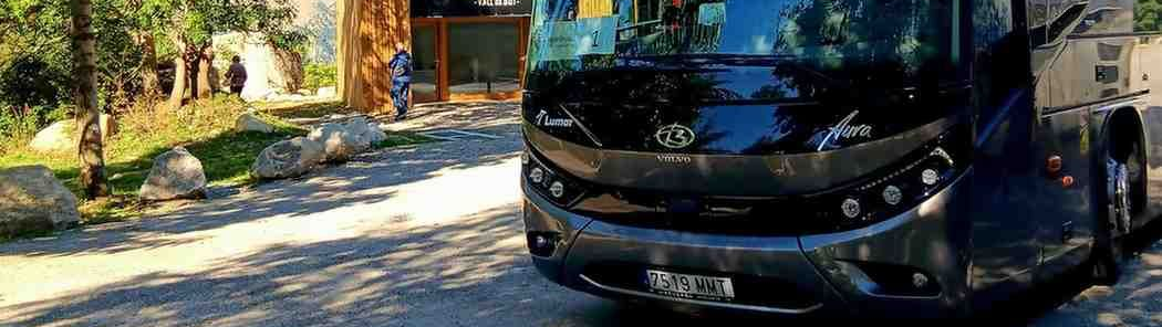 Un autobús turístico de color gris oscuro estaba estacionado en un camino de grava cerca de un edificio.