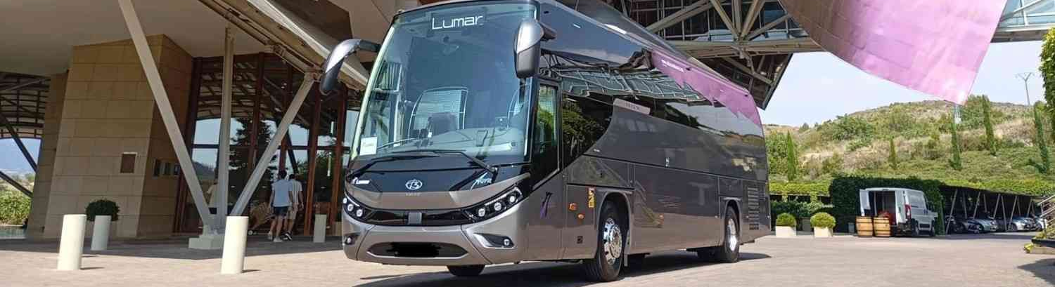 Un autobús turístico moderno de color gris oscuro estaba estacionado frente a un edificio contemporáneo.