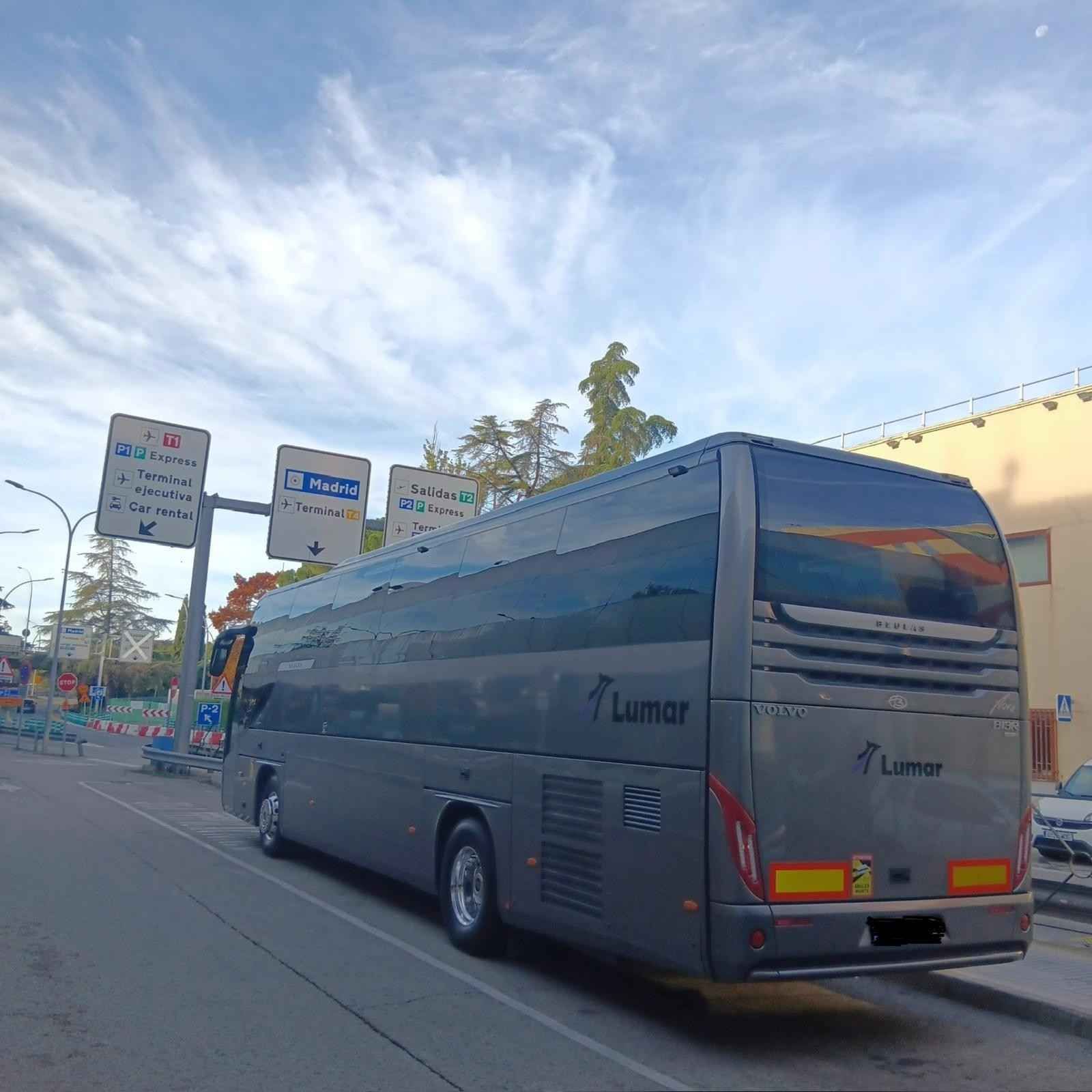 Un autobús gris estacionado al costado de una carretera cerca de señales de tráfico bajo un cielo azul.