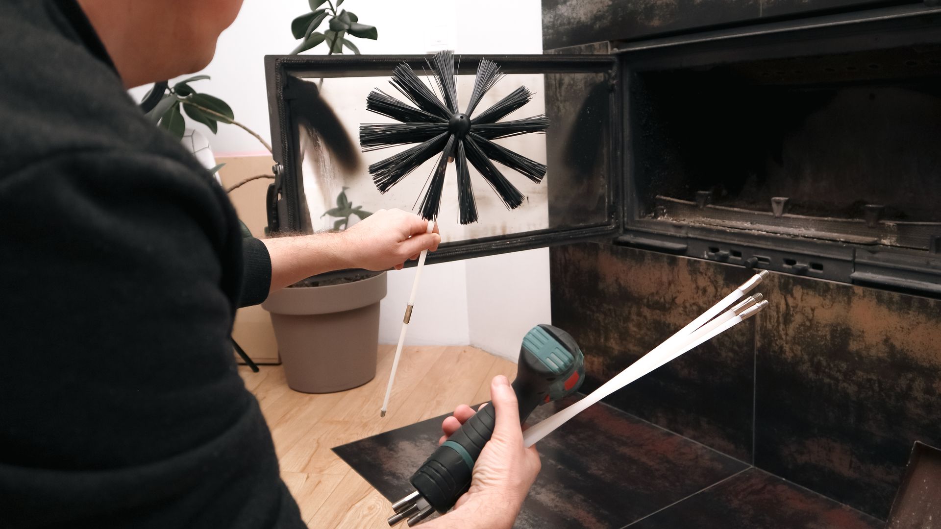 Une personne tenant un outil métallique et inspectant l'ouverture d'un radiateur ou d'une cheminée noire fixée au mur.