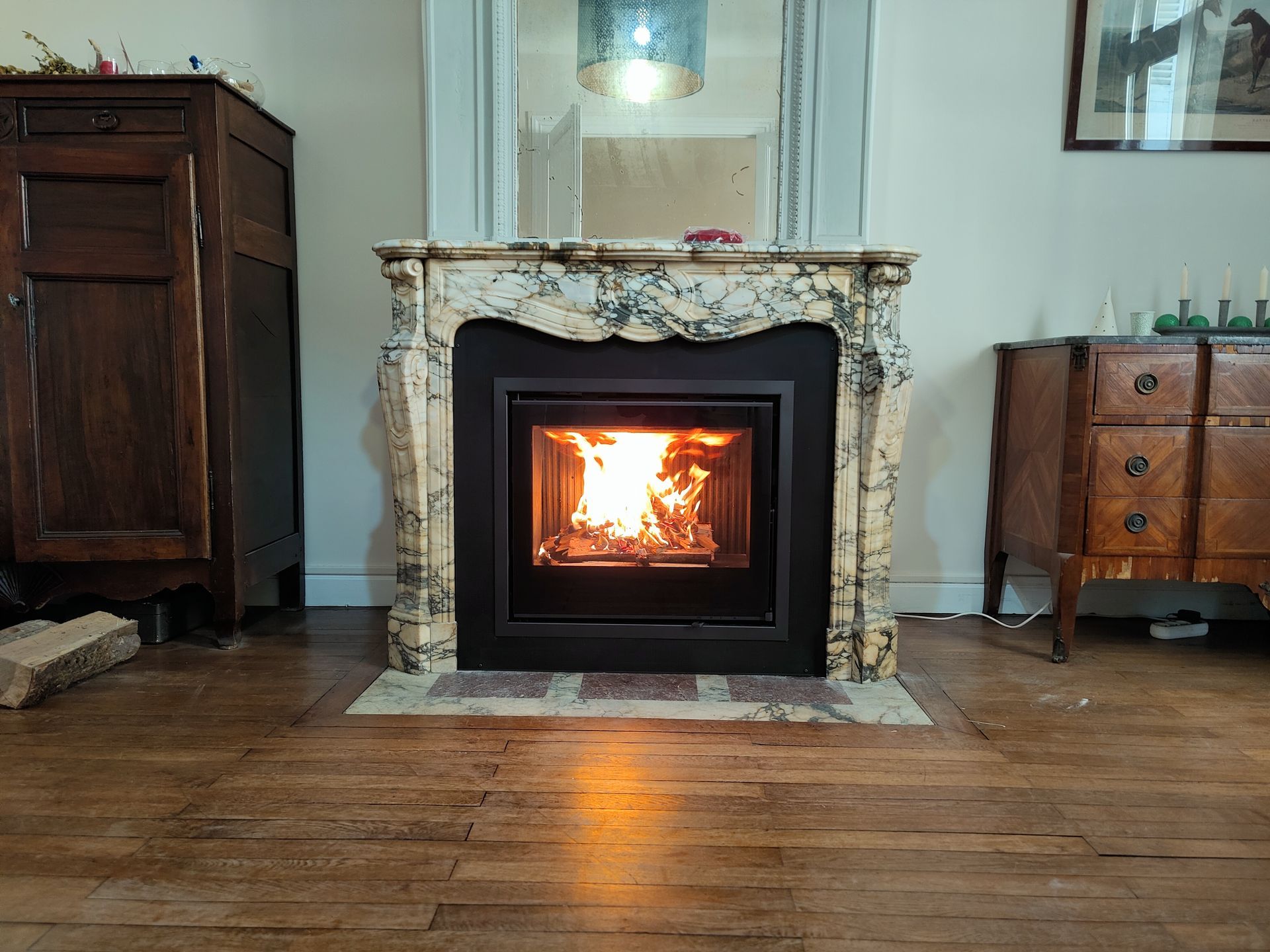 Salon chaleureux avec une cheminée allumée centrée sur un manteau en pierre et un parquet.