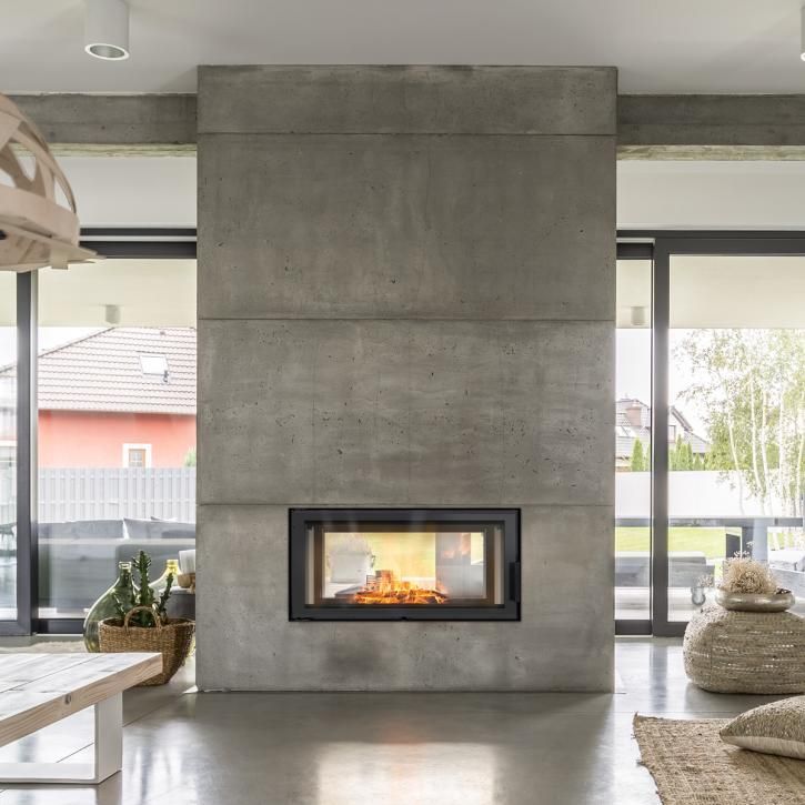 Salon moderne avec une grande cheminée en béton et un feu, encadré par des baies vitrées allant du sol au plafond