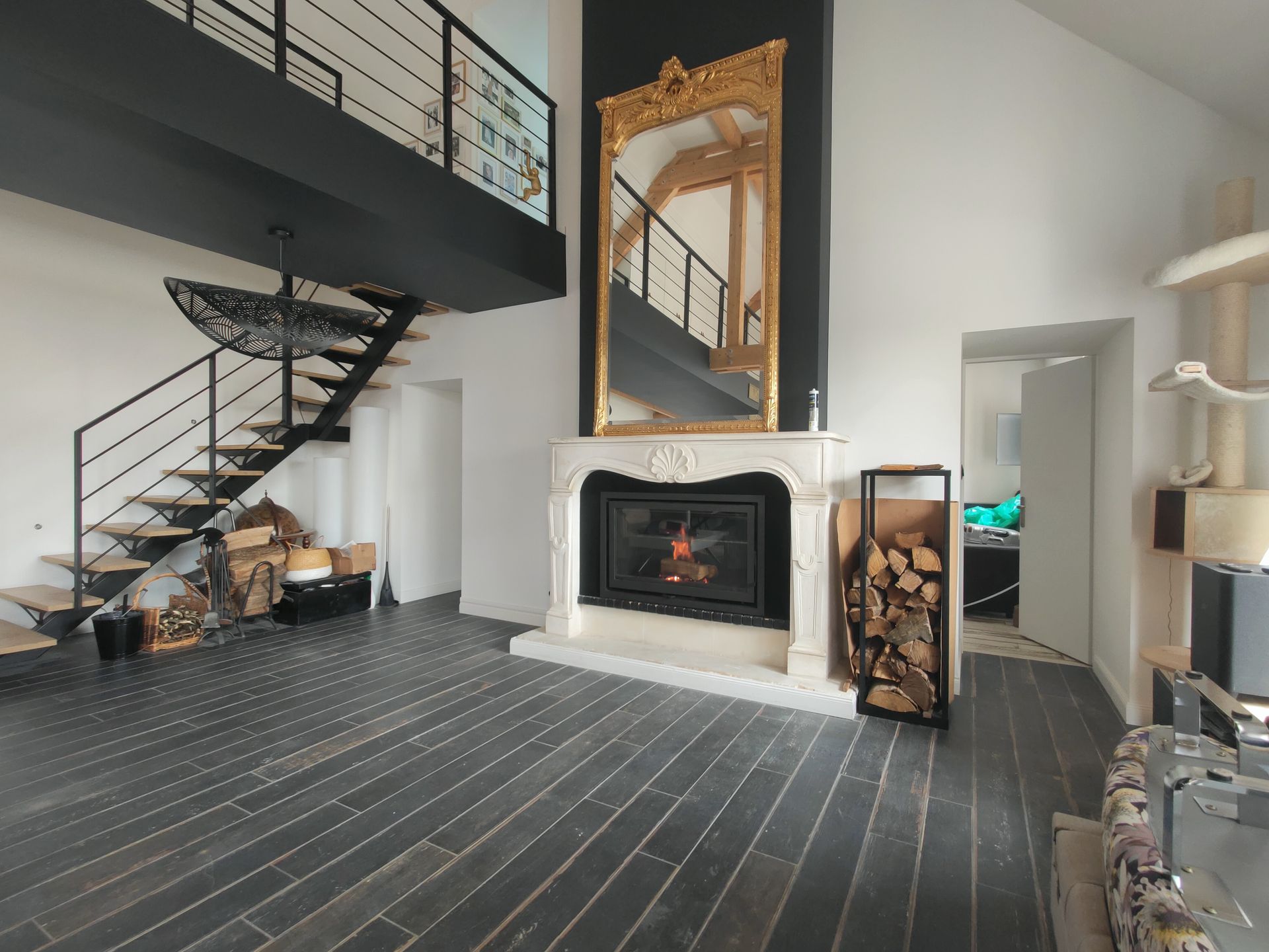 Salon moderne de style loft avec escalier noir, cheminée et grand miroir encadré d’or