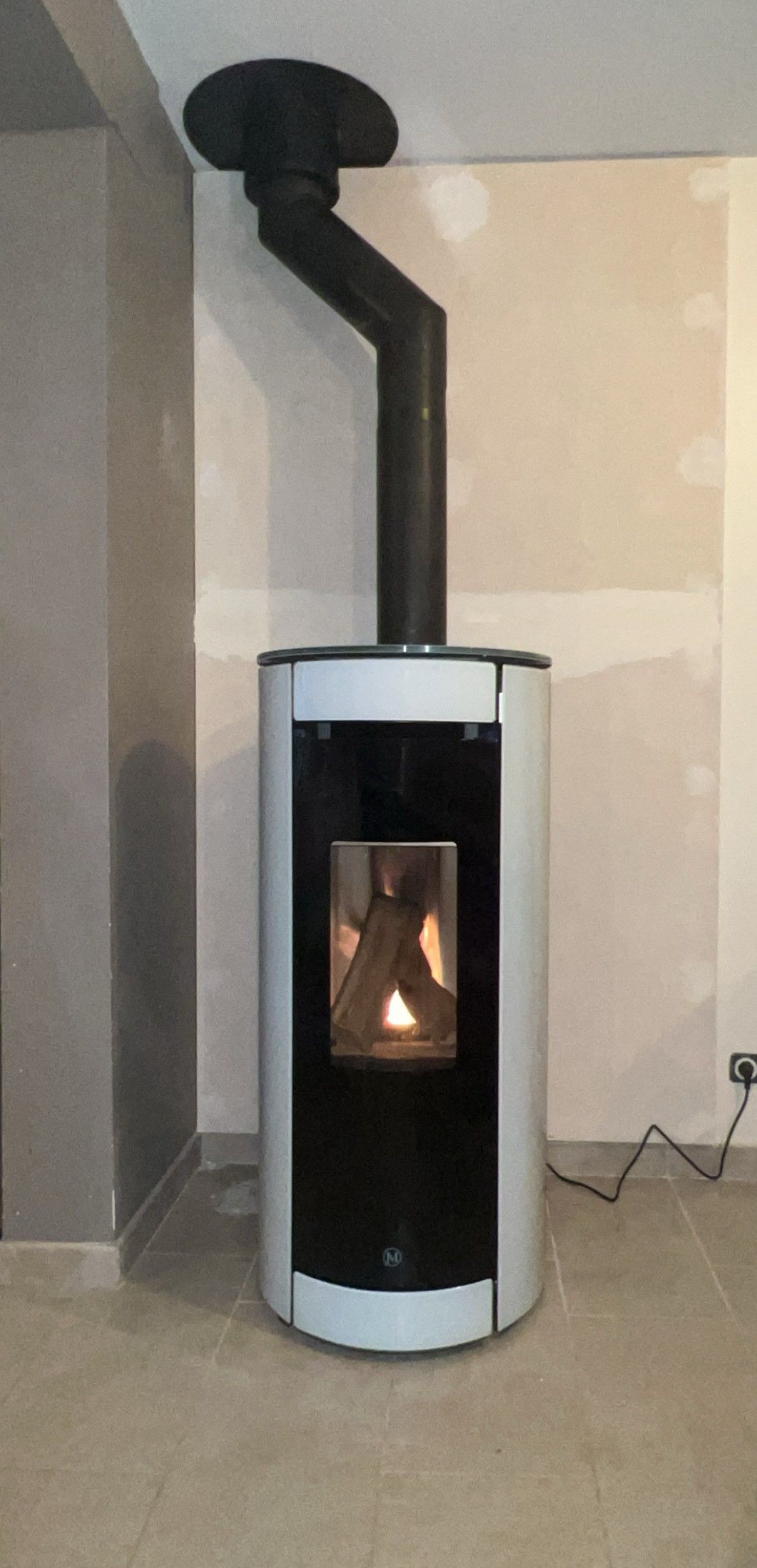 Poêle à bois cylindrique blanc avec conduit de fumée noir dans un coin de pièce