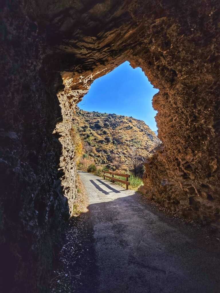 Túnel que da a un sendero de montaña, cielo azul brillante visible.