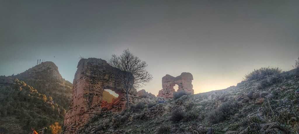 Formaciones rocosas en ruinas con arcos, recortadas contra un cielo crepuscular. La vegetación cubre el primer plano.