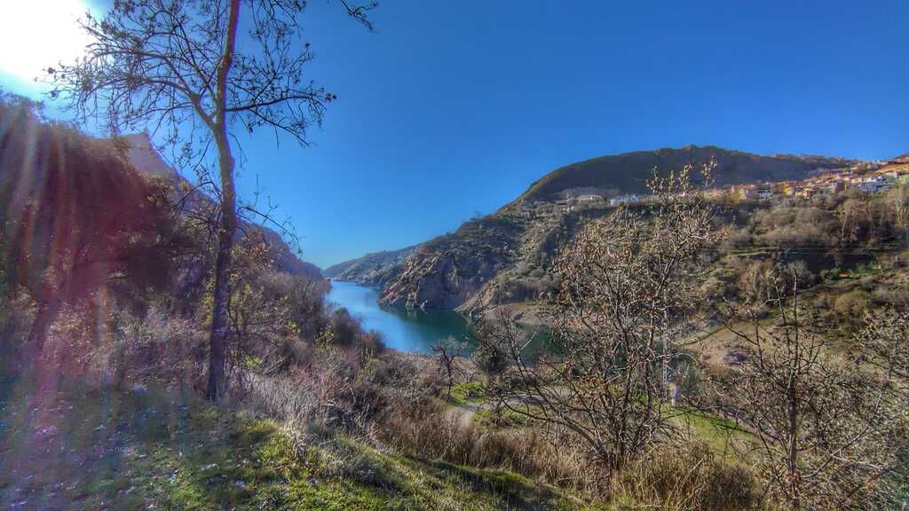 Un cielo azul brillante sobre un lago rodeado de montañas y árboles dispersos.
