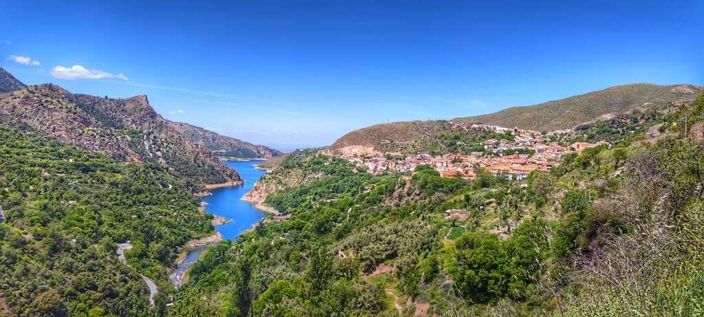 Vista panorámica de un río azul que serpentea a través de un cañón rodeado de árboles verdes y formaciones rocosas bajo un cielo azul despejado.