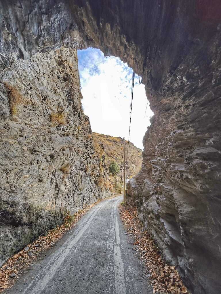 Carretera excavada en la roca, con el cielo visible sobre nuestras cabezas. Hojas marrones a los lados del camino.