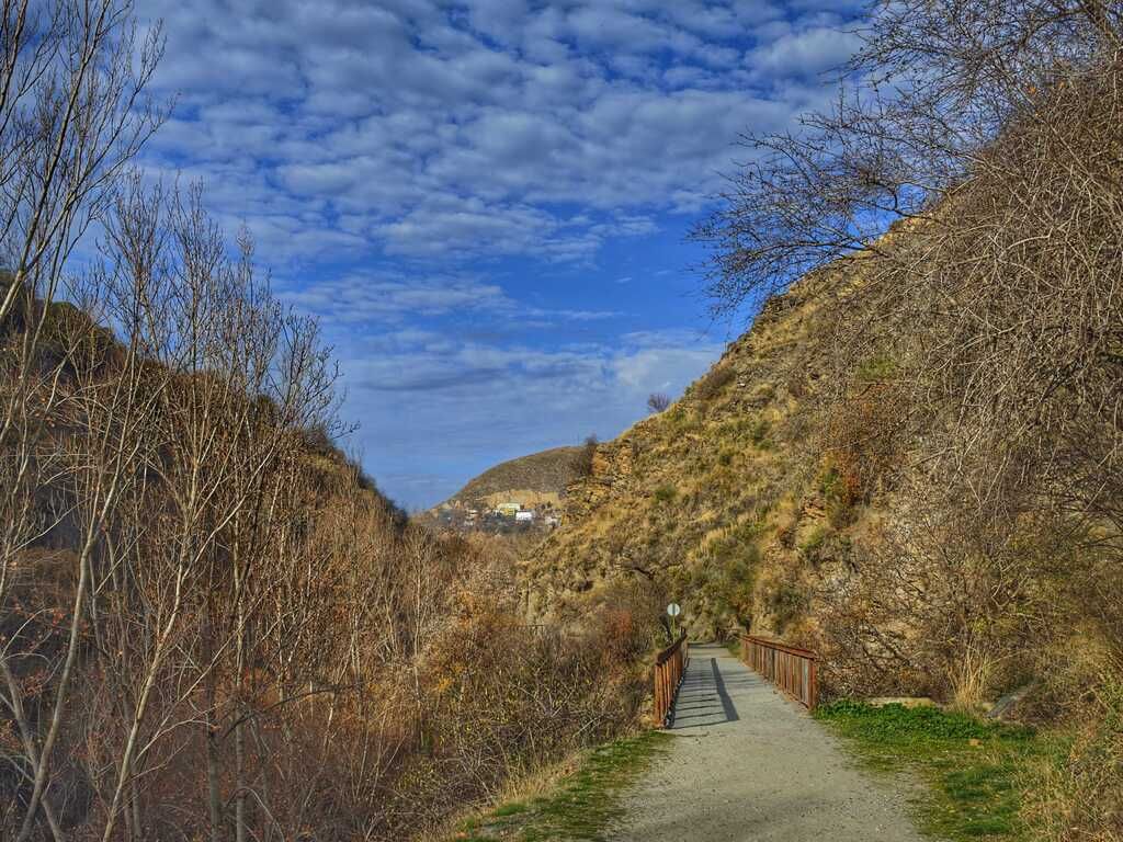 Sendero a través de un paso de montaña con escasa vegetación bajo un cielo azul parcialmente nublado.