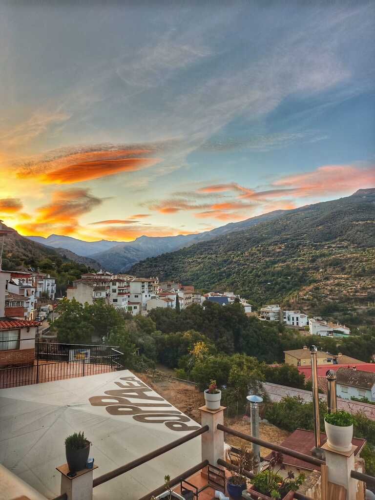 Vista de un pueblo blanco enclavado entre montañas verdes bajo un cielo de atardecer naranja y azul.