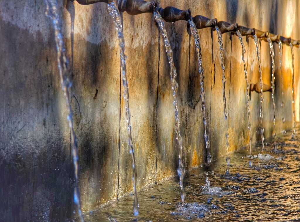 Agua que cae en cascada desde múltiples surtidores en una pared erosionada, luz dorada del sol.