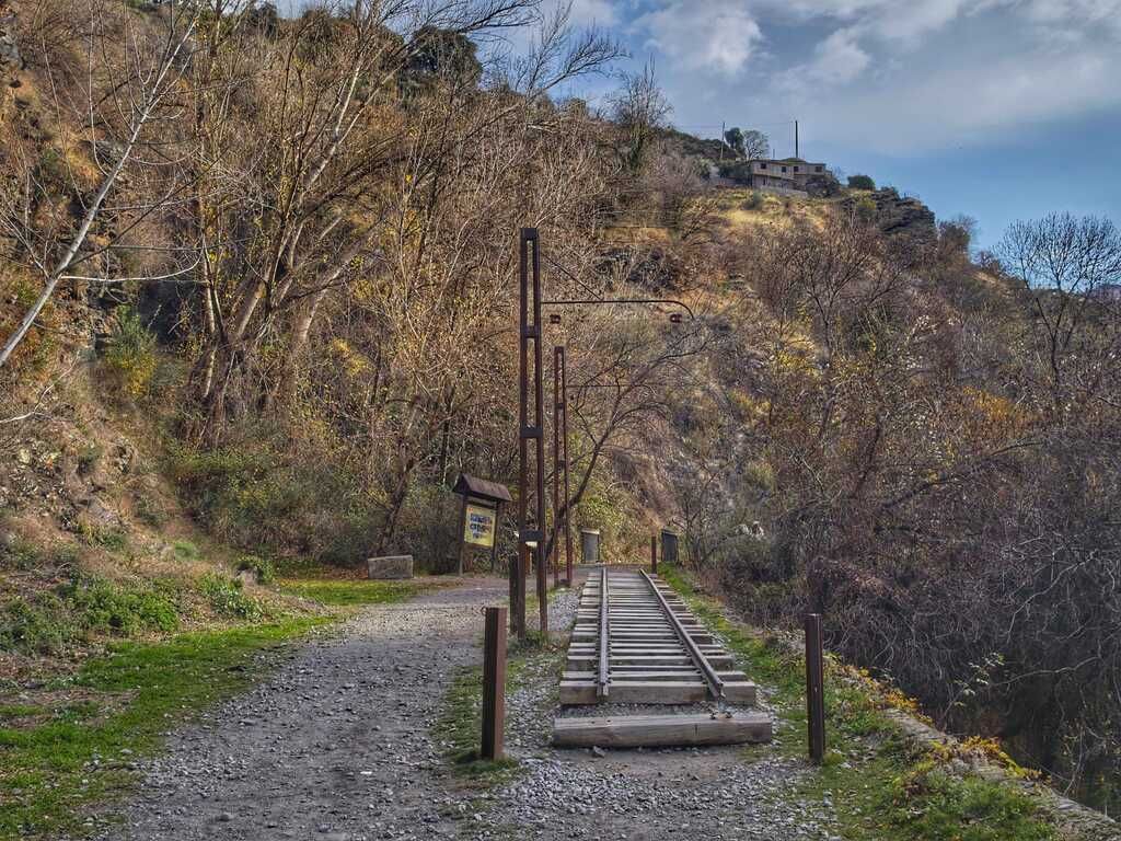 Un sendero de grava con vías de ferrocarril de madera conduce a la ladera de una colina, con árboles a ambos lados.
