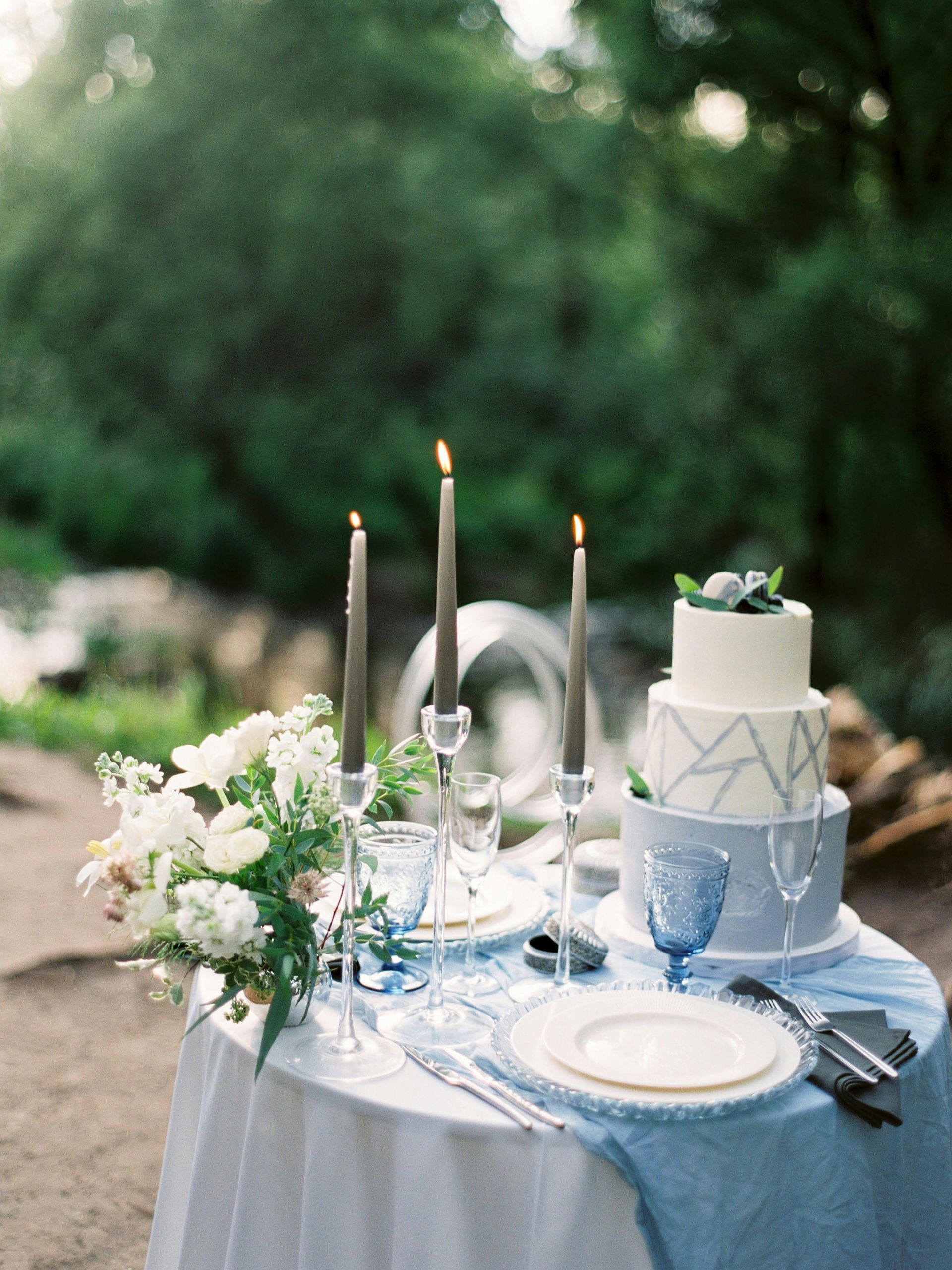 Elegante mesa de boda al aire libre con pastel, flores, velas y detalles azules.