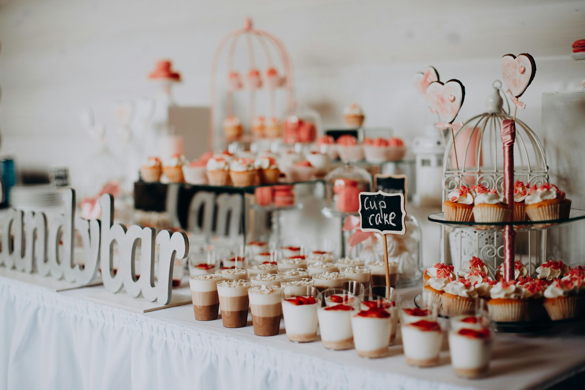 Mesa de postres con cupcakes, macarons y capas de dulces en color rosa y blanco