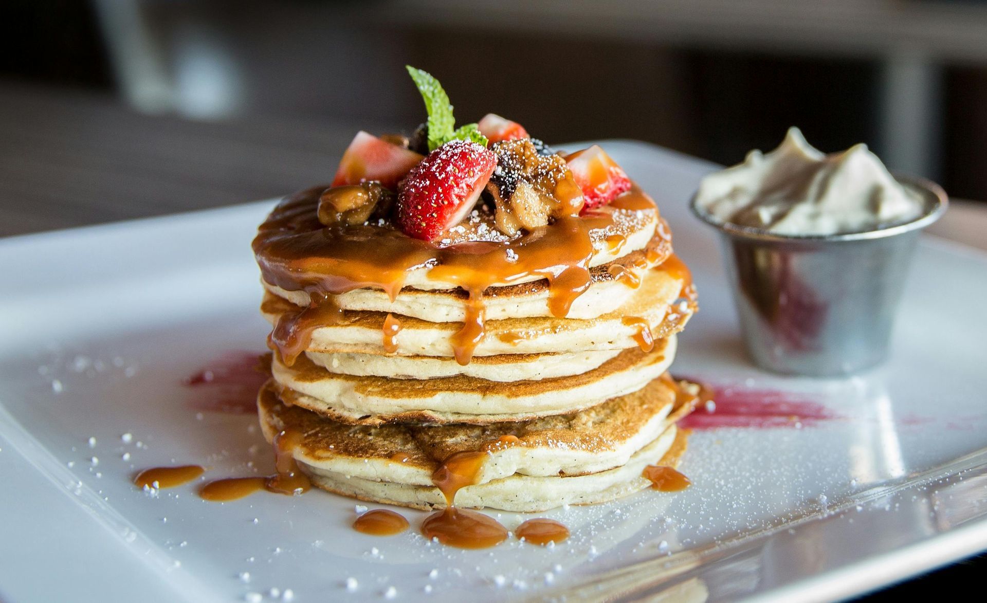 Pila de panqueques cubiertos con fresas, nueces y salsa de caramelo, servidos con crema batida.