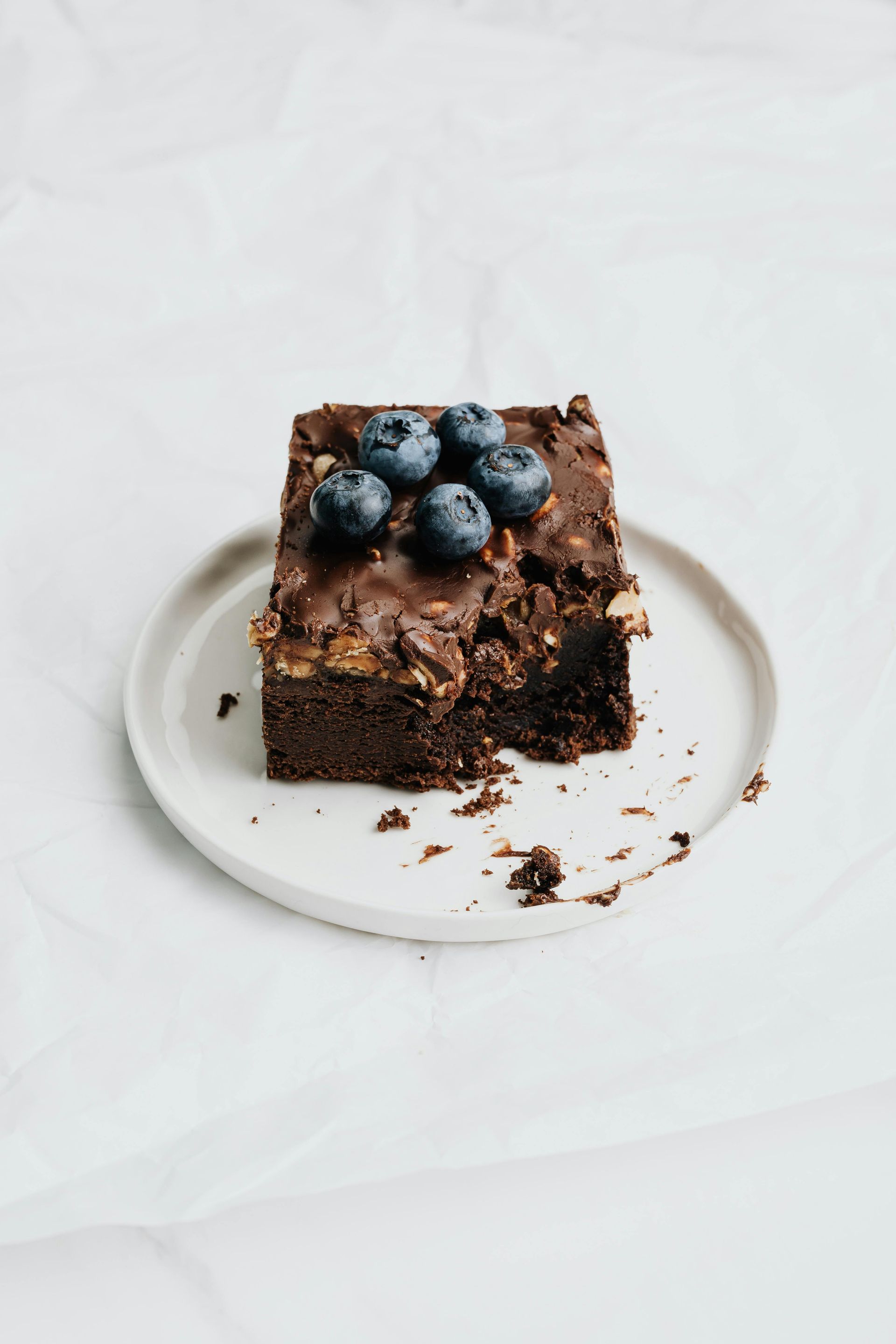 Brownie de chocolate con arándanos en un plato blanco, fondo blanco.