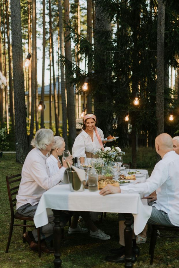 Una familia se reúne para comer al aire libre en un bosque. Una mujer sirve la comida en la mesa.