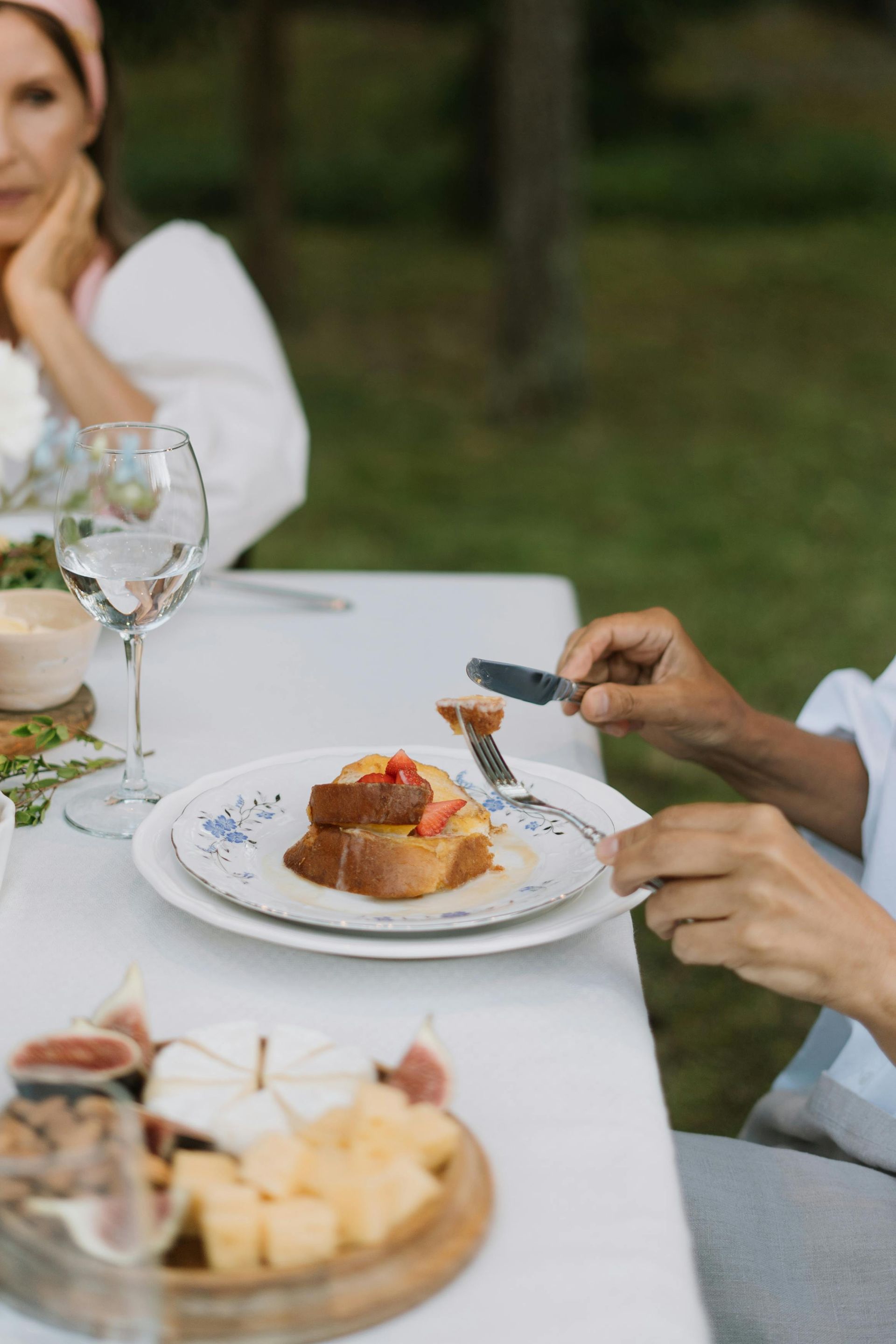 Persona comiendo en una mesa al aire libre. Varios platos y una mujer al fondo.