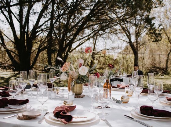 Mesa de recepción de boda al aire libre con centro de mesa floral y detalles en color burdeos.