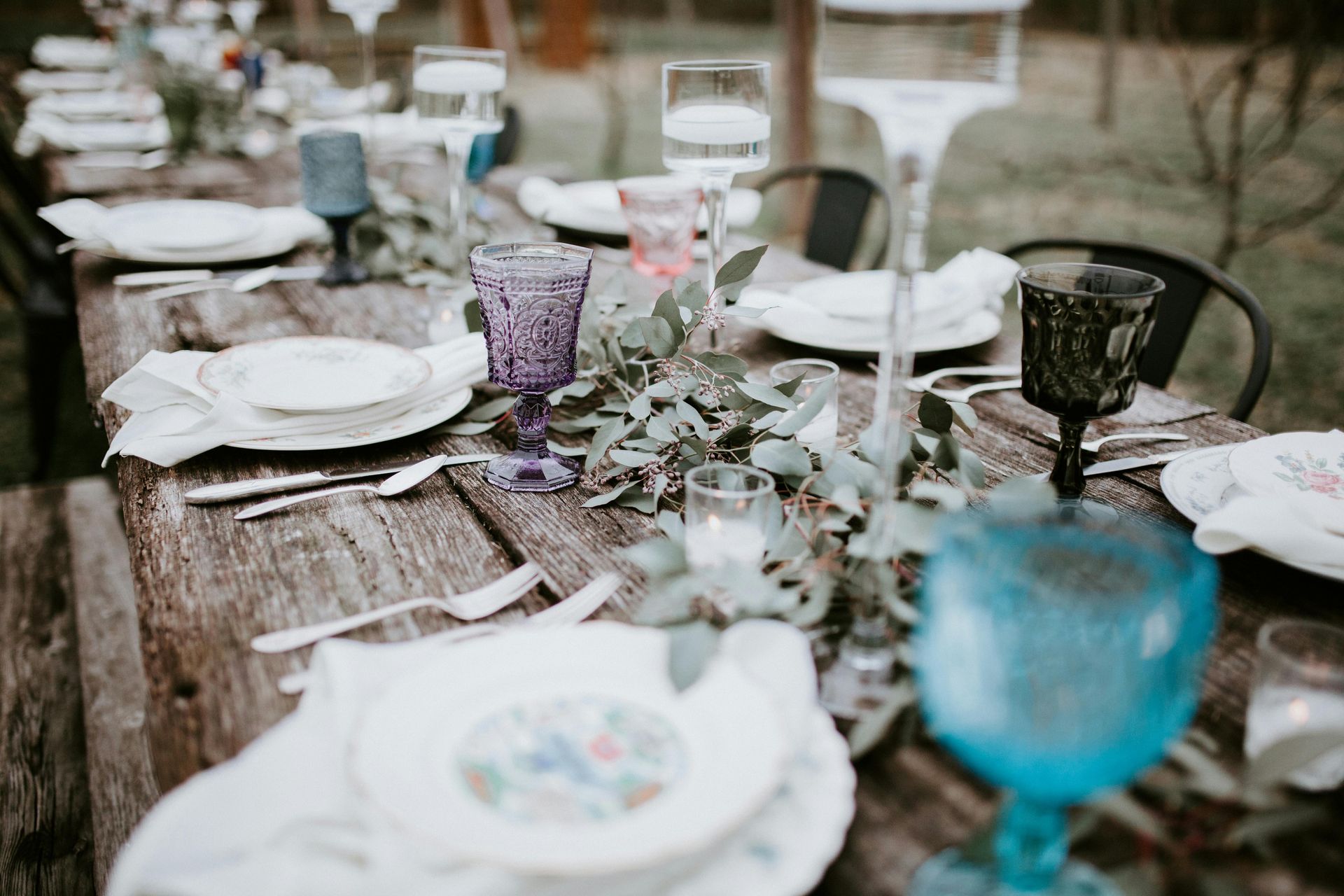 Juego de mesa de madera rústica para una reunión, con arreglos florales, cristalería