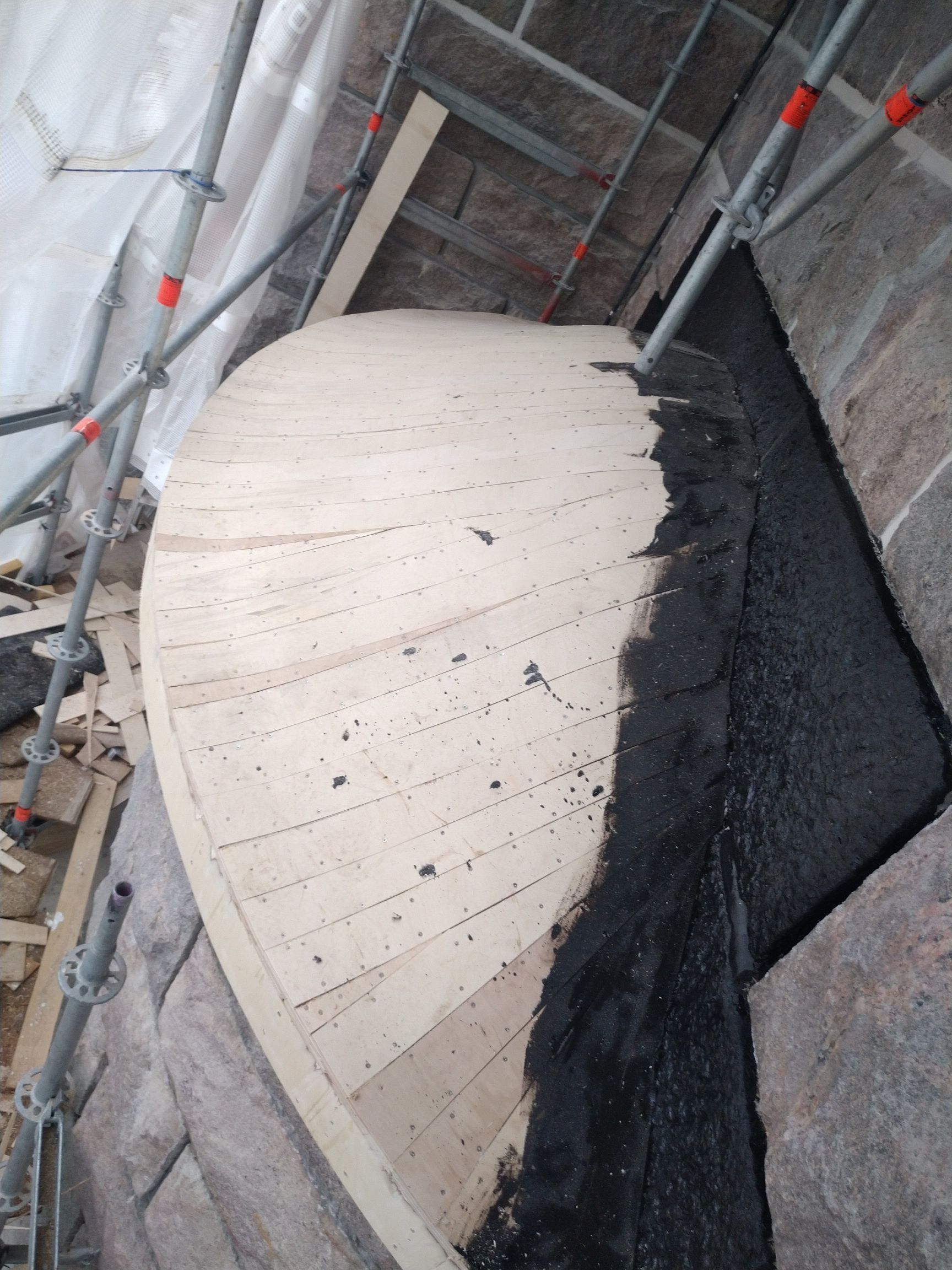 Kaareva betoninen portaikko rakenteilla, telineillä ja paljaalla mustalla vedeneristysmateriaalilla