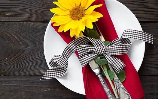 Un plato blanco con una servilleta roja y una flor amarilla encima.