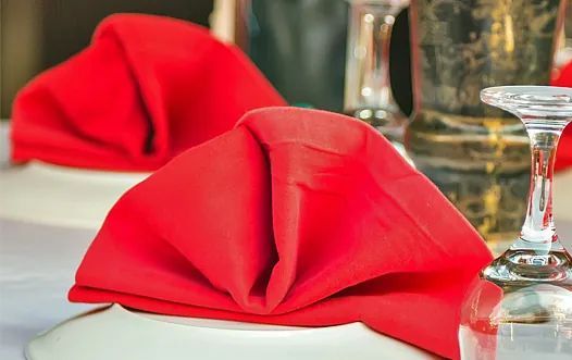 Una servilleta roja está sobre un plato blanco al lado de una copa de vino sobre una mesa.