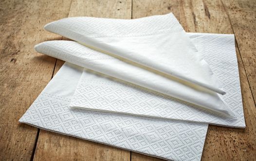 Tres servilletas blancas están apiladas una encima de otra sobre una mesa de madera.