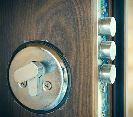 Primer plano de una cerradura de puerta de madera con un cerrojo plateado y tres pestillos metálicos.