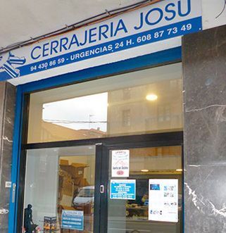 Fachada de la cerrajería Cerrajería Josu, con letrero azul y entrada de cristal en una esquina.