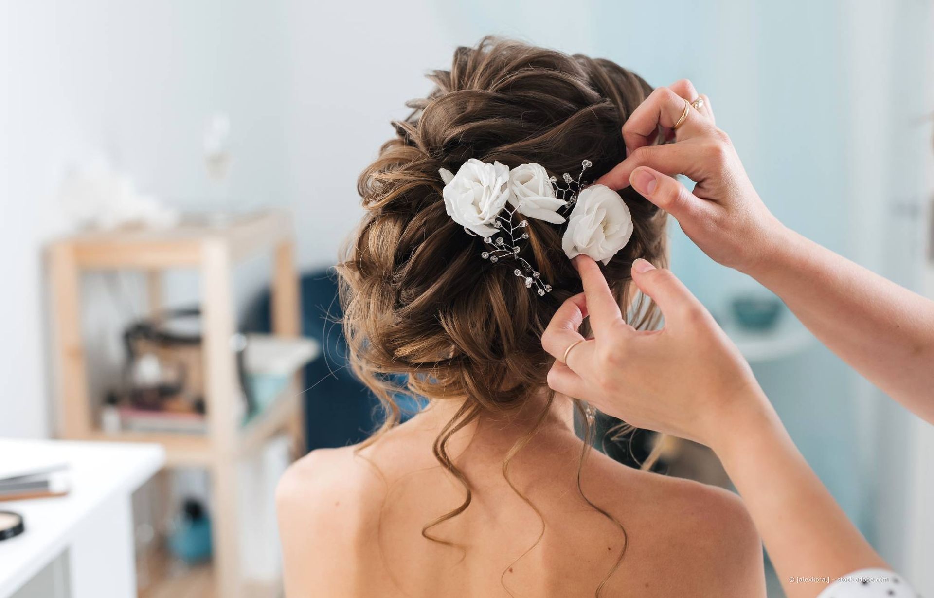 Eine Friseurin befestigt florale Haaraccessoires an der Hochsteckfrisur einer Frau.