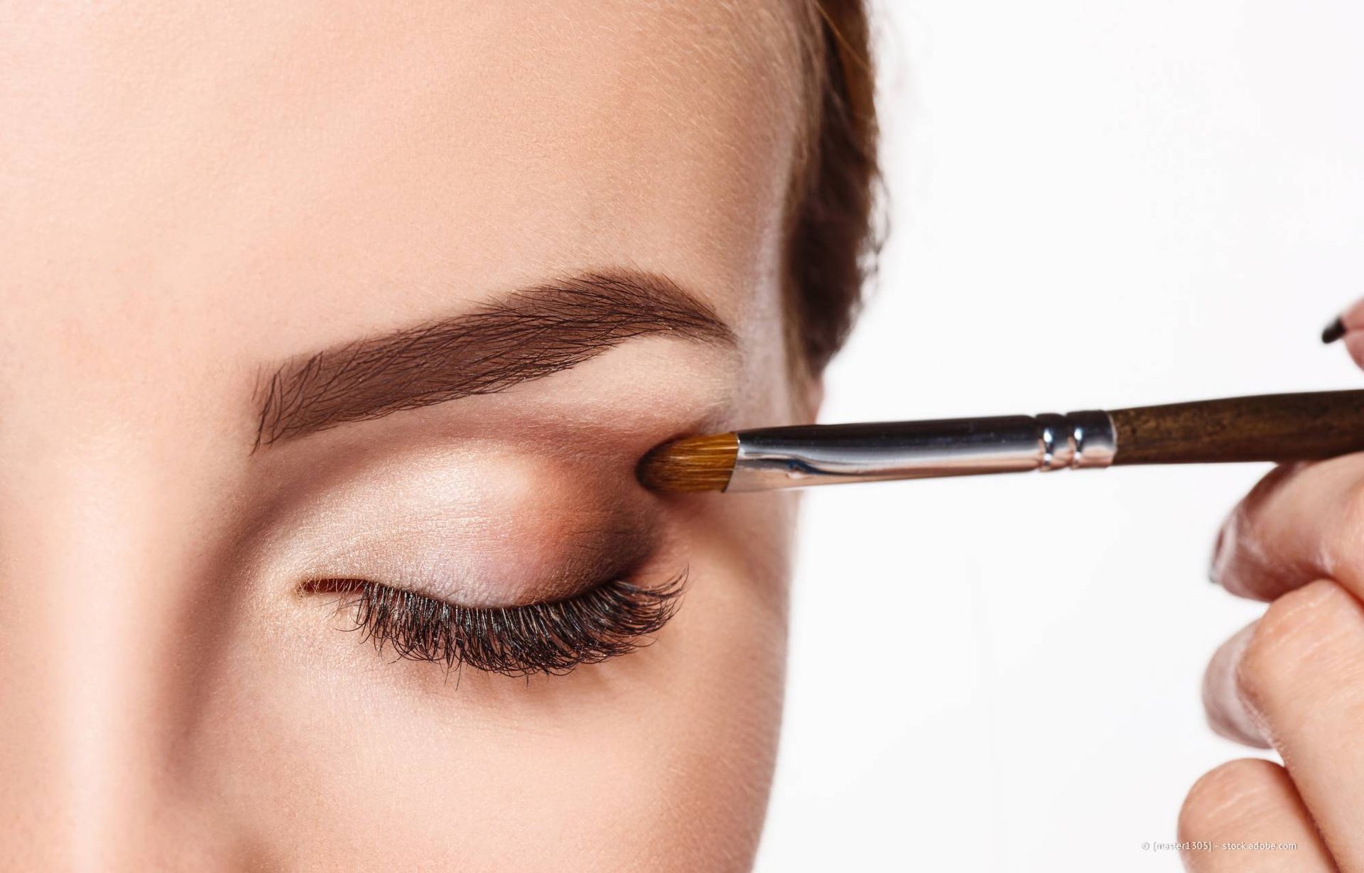 Visagistin trägt Lidschatten auf ein geschlossenes Auge auf.