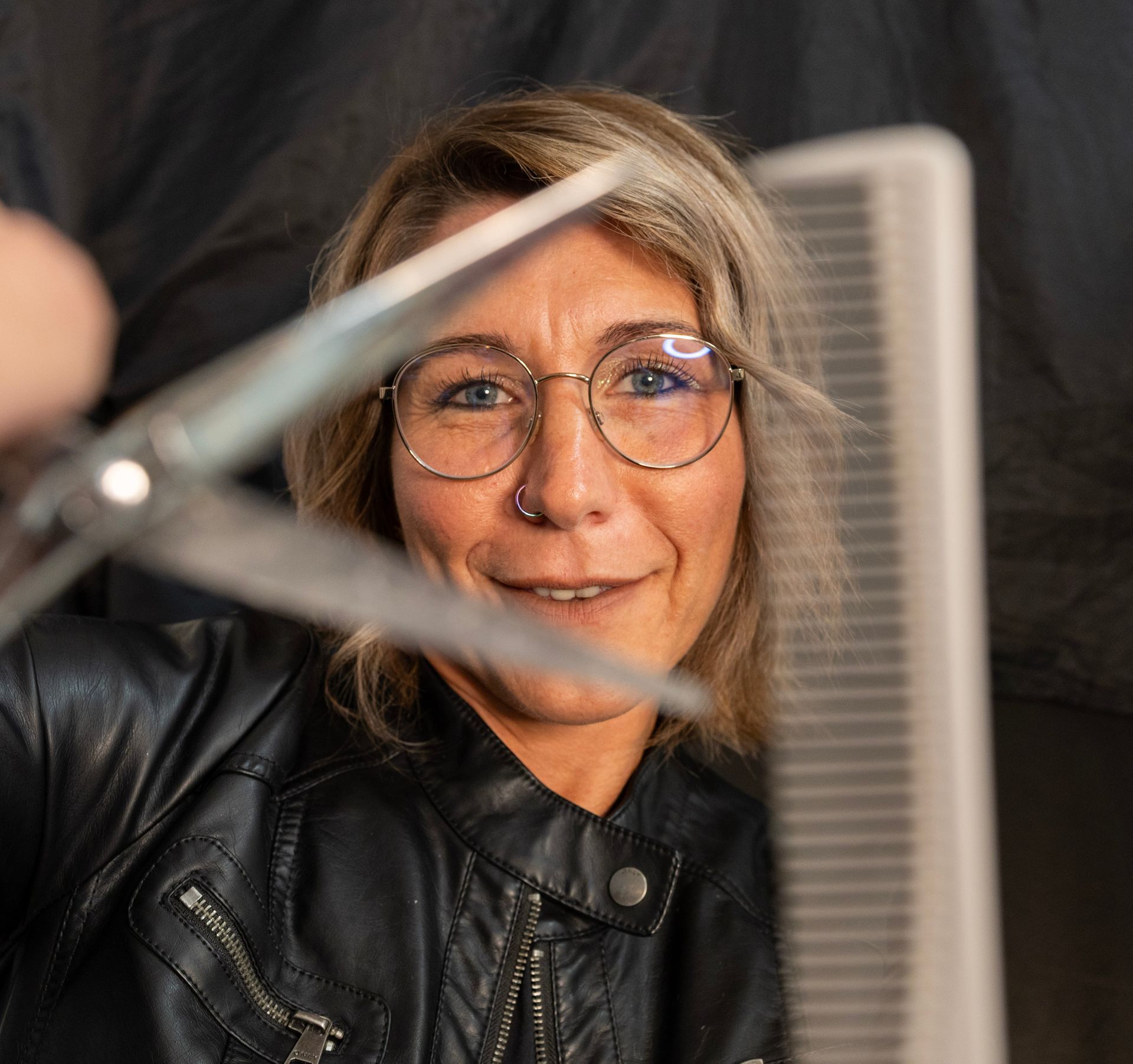 Frau mit Brille hält Schere und Kamm, im Begriff, Haare zu schneiden.