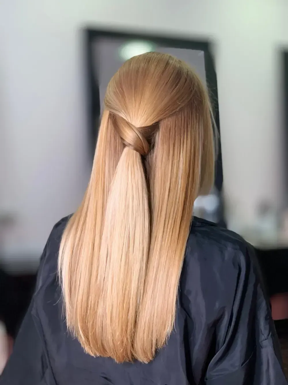 Cabello rubio en un peinado retorcido medio recogido con capas largas y rectas, visto desde atrás.