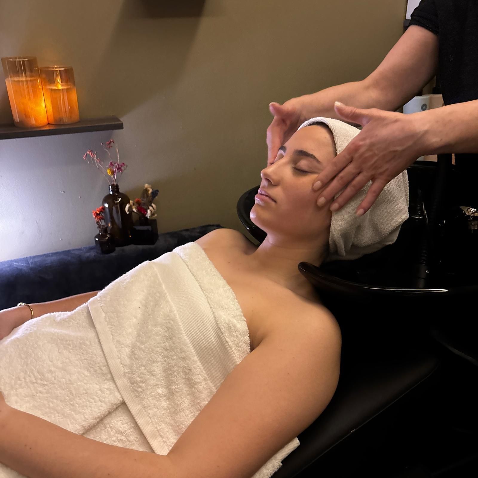Mujer recibiendo un masaje facial en un spa, con una toalla en la cabeza y sobre el pecho.