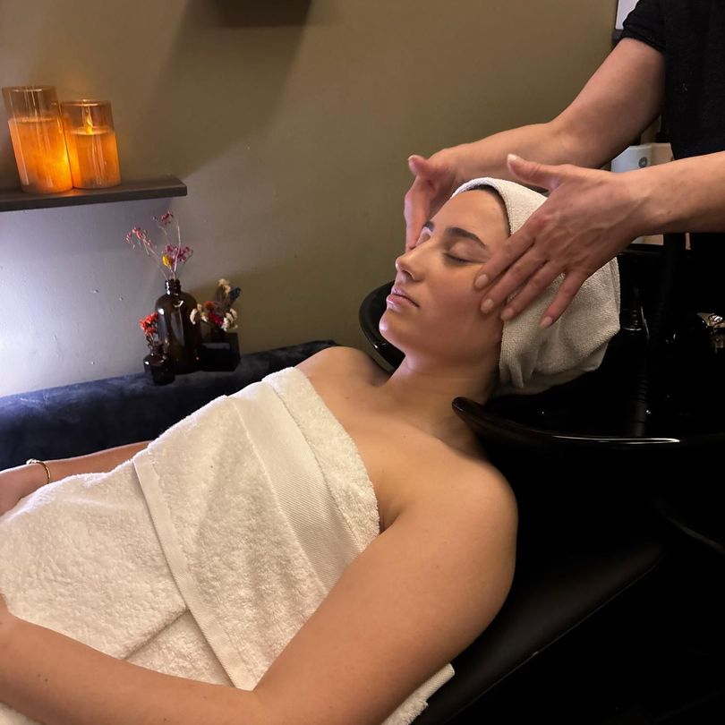 Mujer recibiendo un masaje facial en un spa, con una toalla en la cabeza y sobre el pecho.