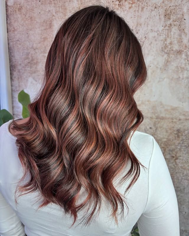 Mujer con cabello castaño largo y ondulado con reflejos rojizos; vista posterior.